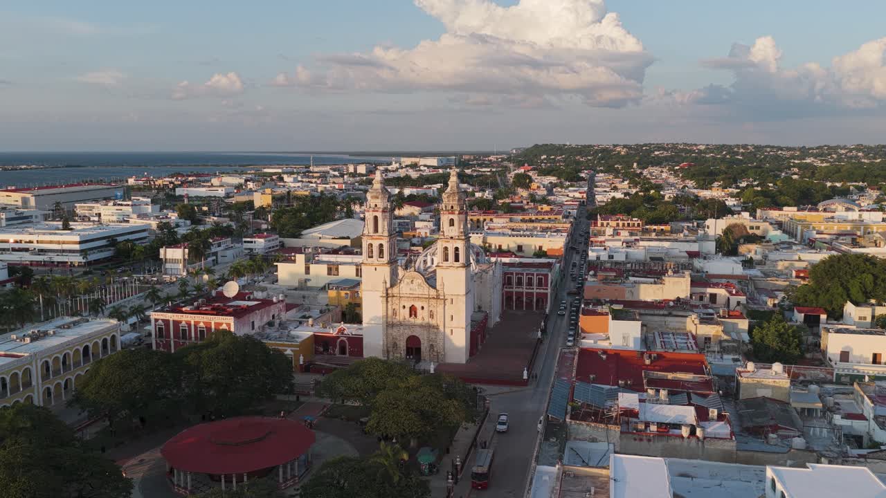 Rising aerial view over Campeche Cathedral, Plaza de la Independencia and colonial cityscape during golden hour