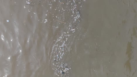 cámara lenta a baja altitud de arriba hacia abajo toma de drone de océano contaminado lleno de basura flotante y escombros y escorrentía de aguas residuales fangosas en bali indonesia