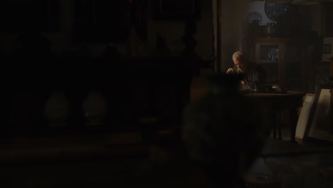 older passionate man evaluates an old silver skull watch in his office at night