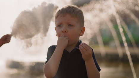 emotional little boy puts hands with candy floss into mouth