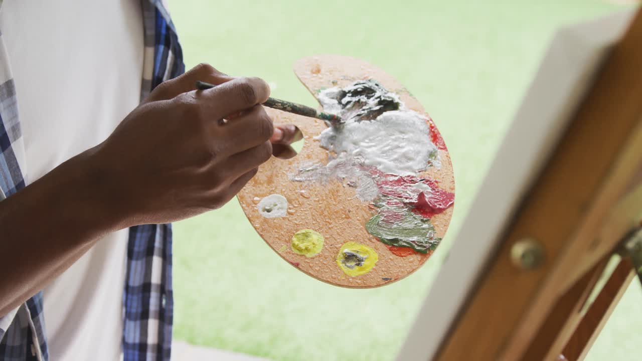 Video of african american senior man painting picture outside