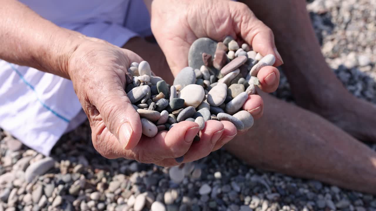 Elderly hands holding pebbles on a beach