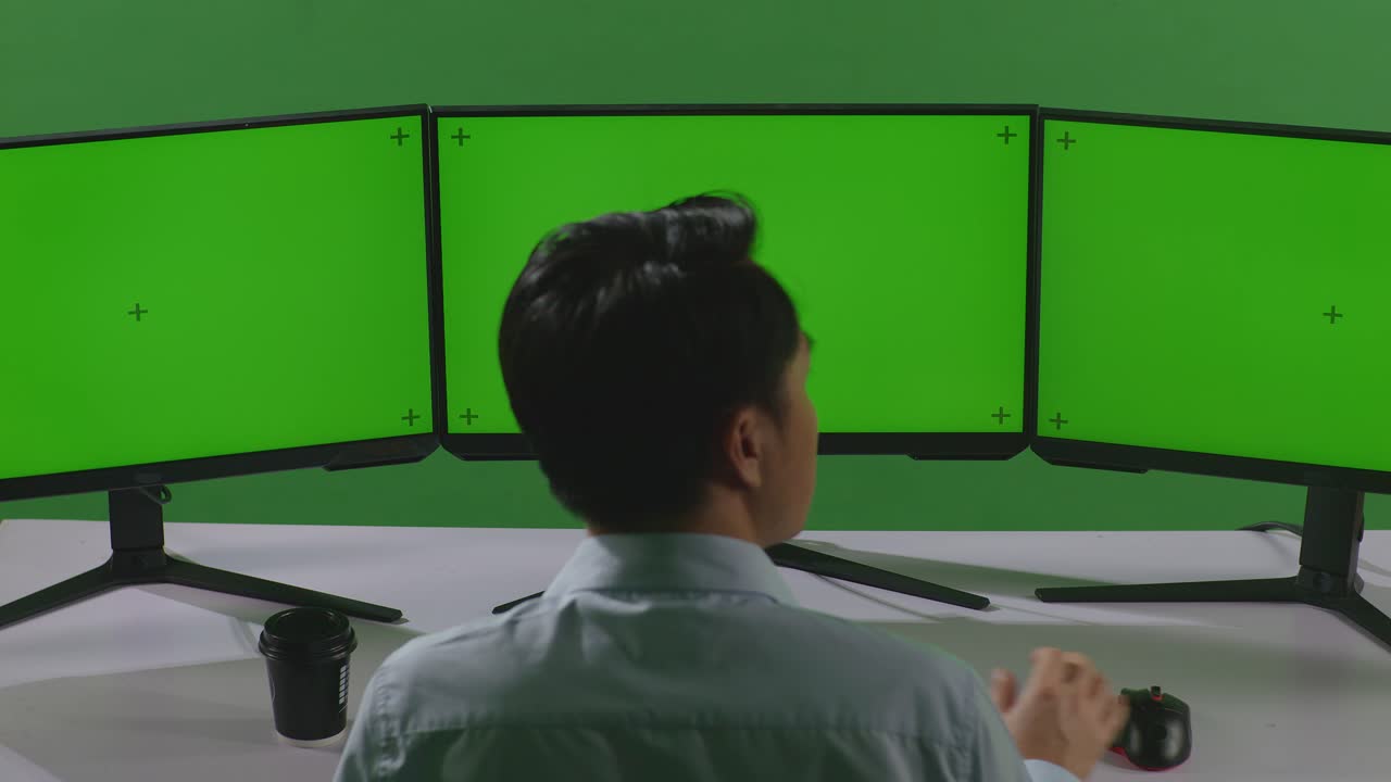 Back View Of Asian Man Thinking About Something Then Raising His Index Finger While Working With Mock Up Multiple Computer Monitor In Green Screen Studio