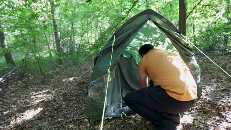 young adult man setting up tent in forest campsite, back slow motion view