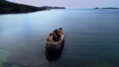 Old rusty shipwreck stuck in shallow water in quiet bay surrounded by green hills abandoned vessel decay in ocean tranquil maritime scenery peaceful atmosphere coastal ship remains