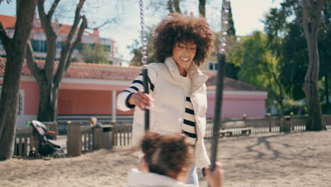 mujer balanceando a su hija en el patio de recreo del parque de cerca. maternidad cariñosa