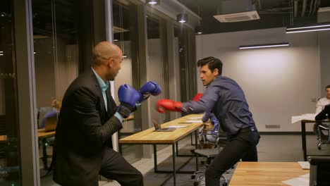 two competitive businessmen fighting with boxing gloves in corporate office