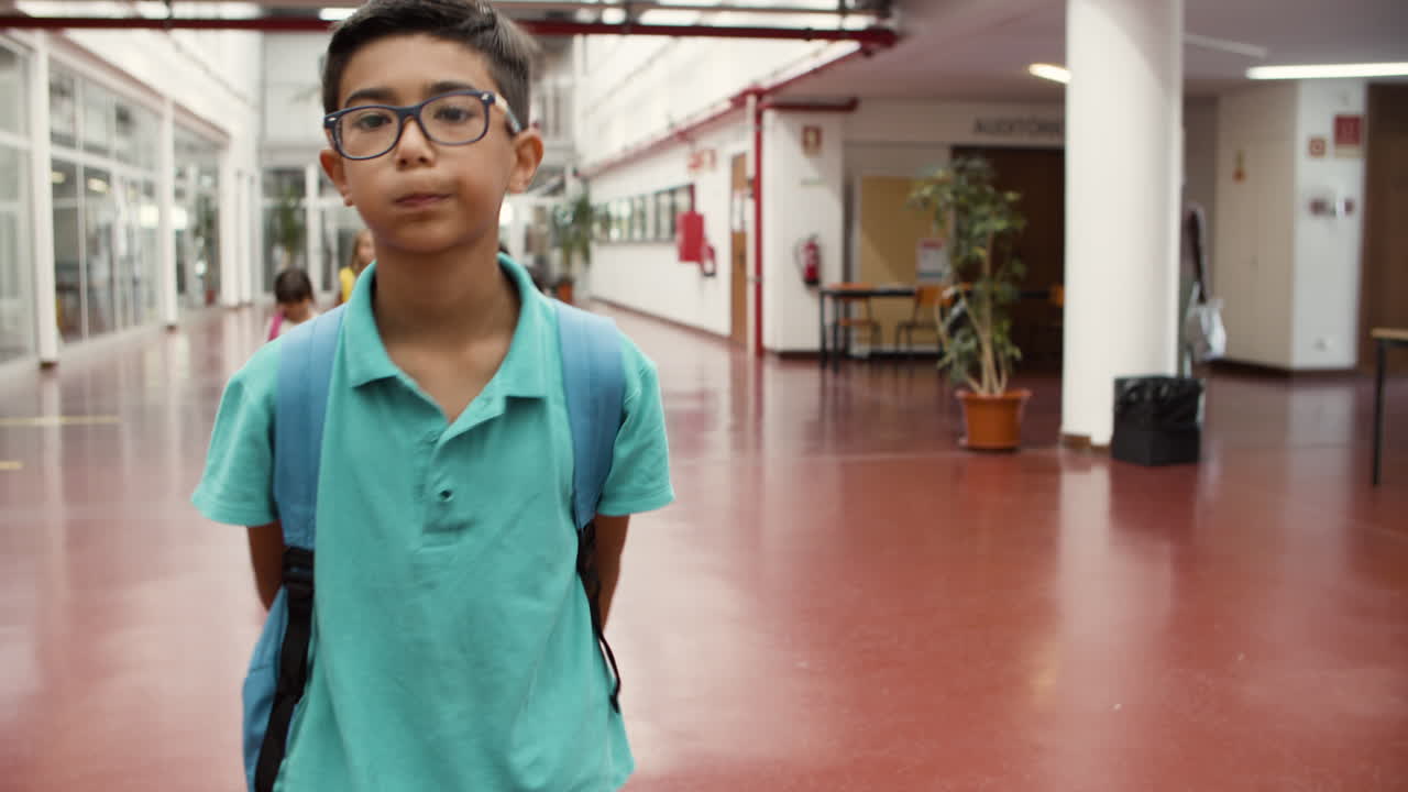 niño con anteojos caminando en el pasillo de la escuela y yendo a clase de mala gana