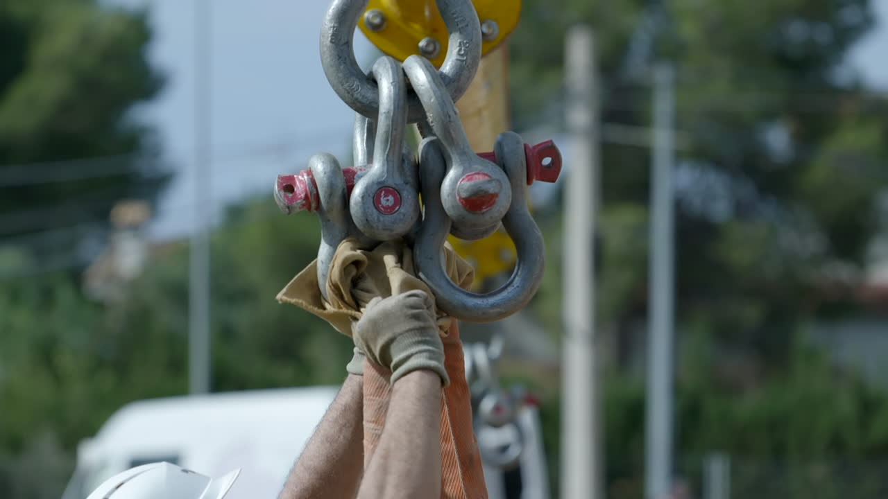 manos de los trabajadores que guían los lazos de bloqueo de acero fuerte suspendidos de la polea de la grúa