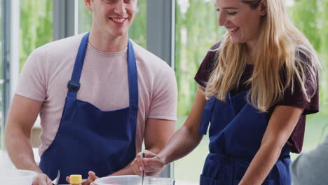 Male-And-Female-Adult-Students-Measuring-Ingredients-In-Cookery-Class-In-Kitchen