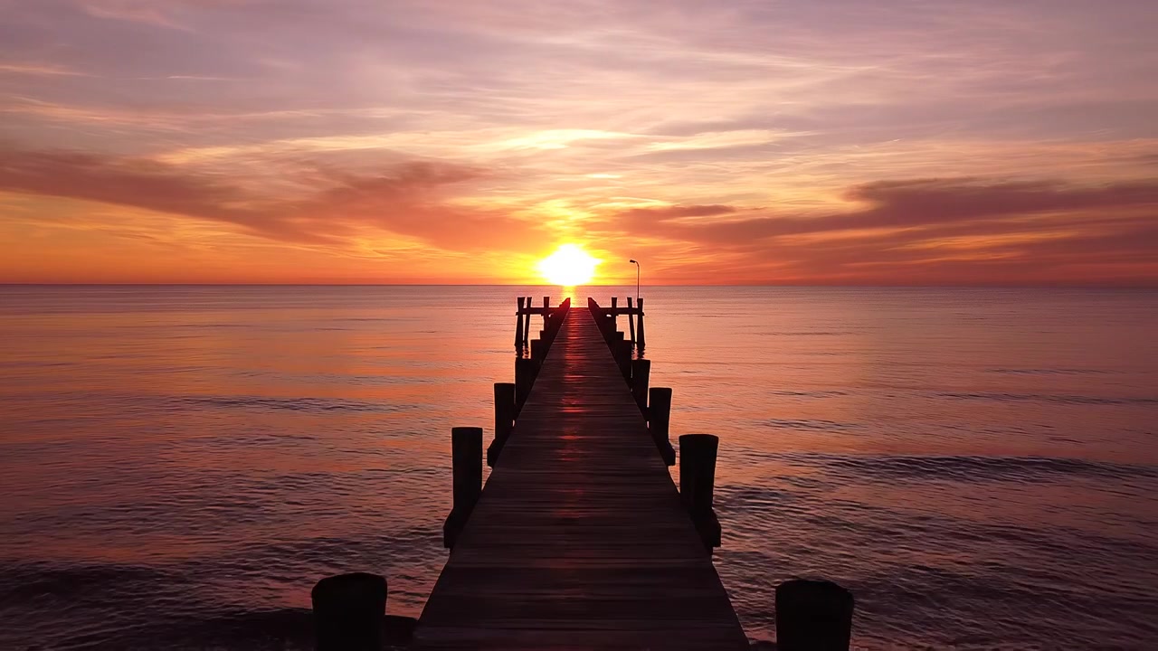Træmole, der fører mod en strålende solnedgang over roligt hav
