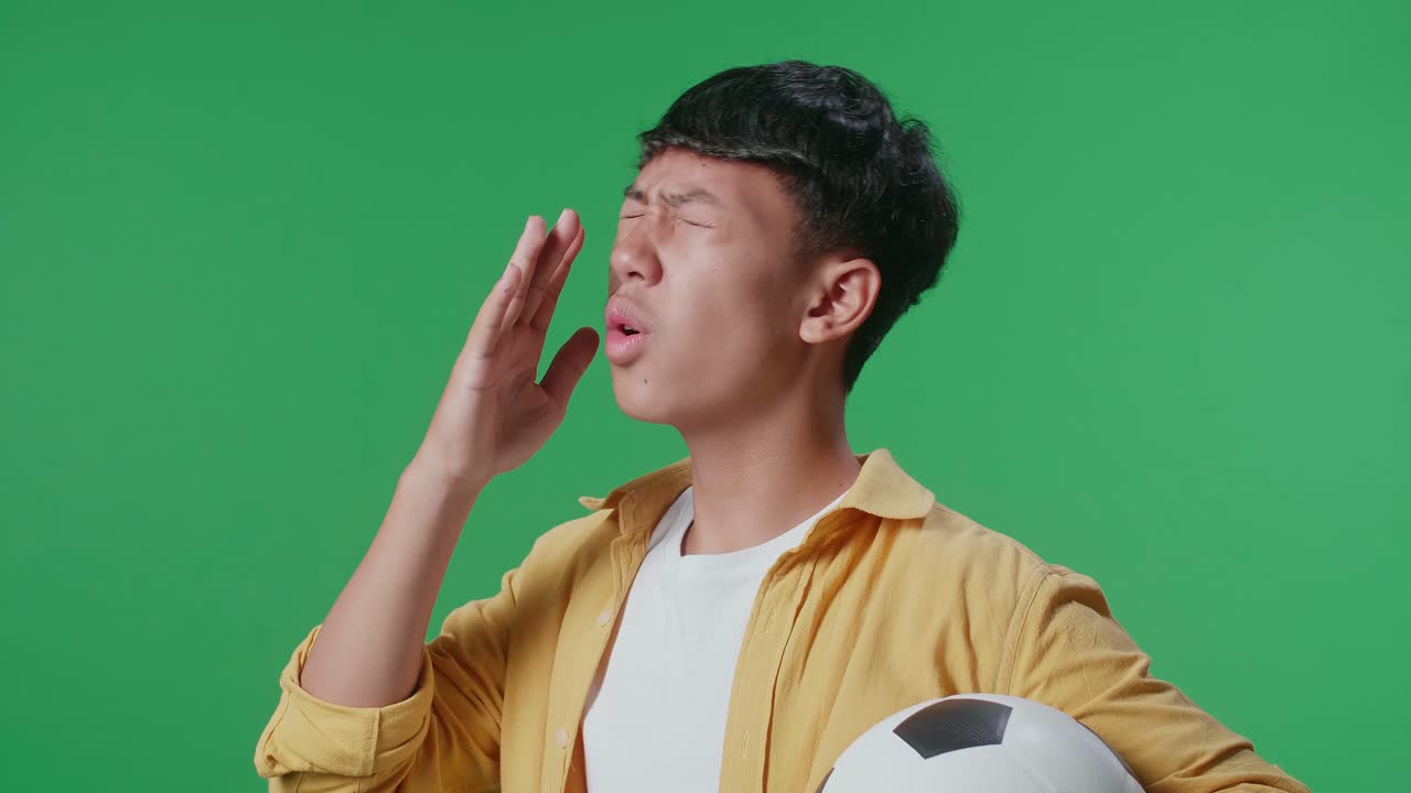 공을 들고 있는 아시아 소년이 골을 고 후회하는 동안 녹색 스크린 배경에서 축구를 응원하는 가까운 측면 뷰