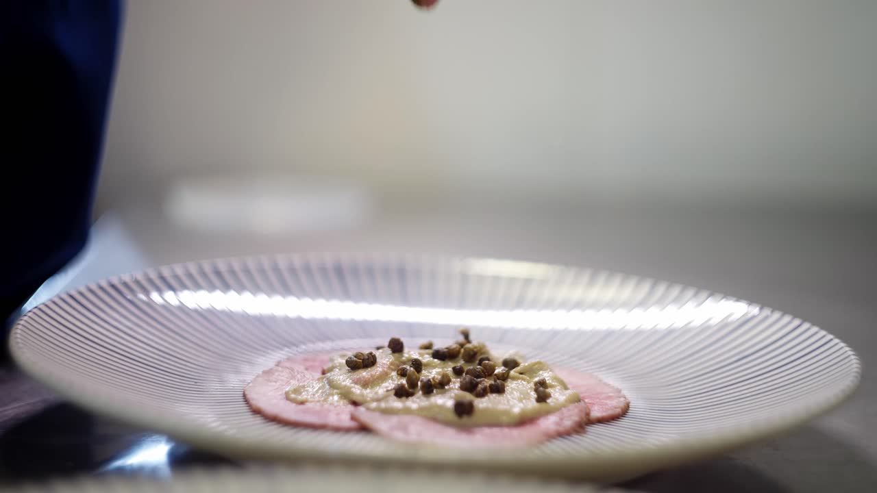 Close up view of a hand spreading green condiment over Vitello Tonnato dish or carpaccio in a fine dining restaurant kitchen