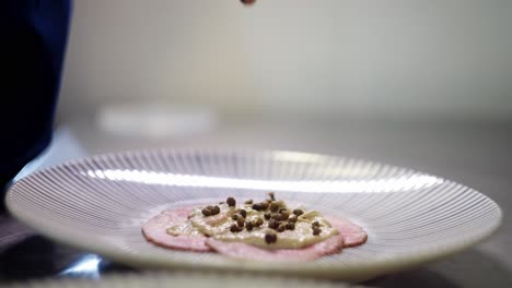 close up view of a hand spreading green condiment over vitello tonnato dish or carpaccio in a fine dining restaurant kitchen
