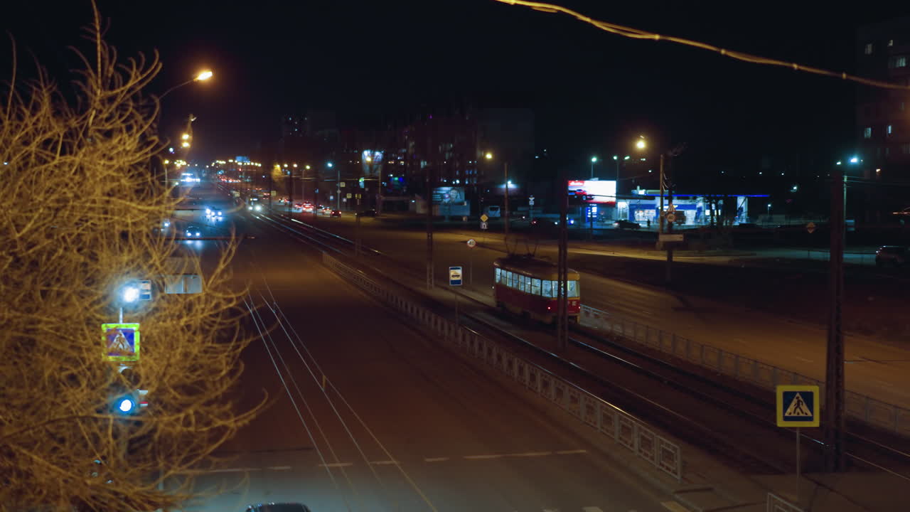 길거리 조명, 건물 및 교통에 둘러싸인 트랙을 따라 이동하는 빨간 트램을 특징으로하는 야간 도시 풍경의 가까운 시각