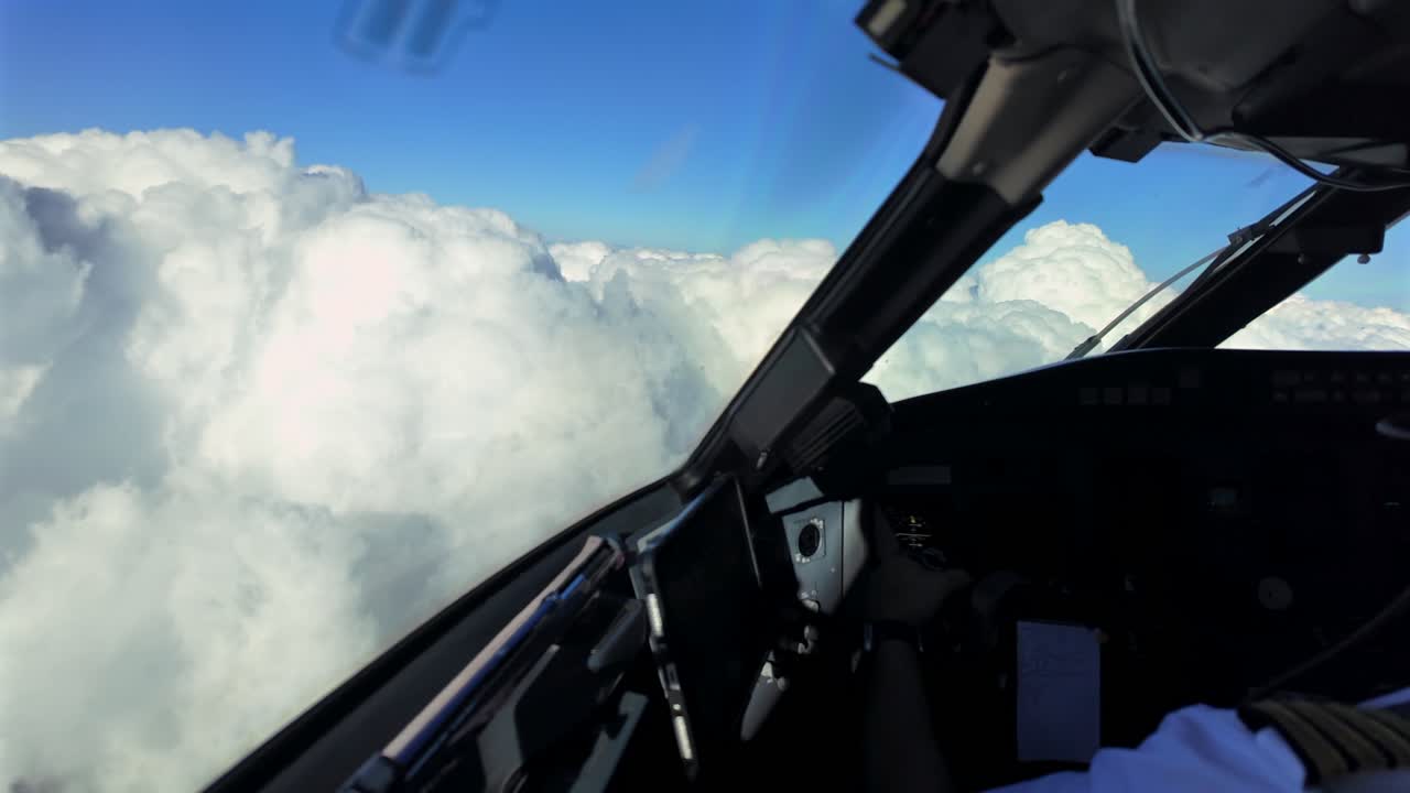 an immersive pilot’s perspective taken from inside a jet cockpit with a partial view of a caucasian pilot seated in the Captain seat, flying manually over a sea of threatening storm clouds. 4K