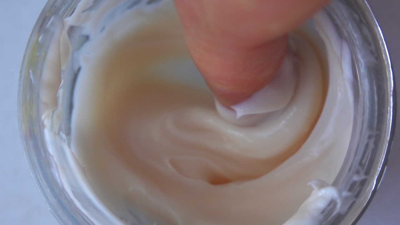 Woman finger picking up cream from a jar