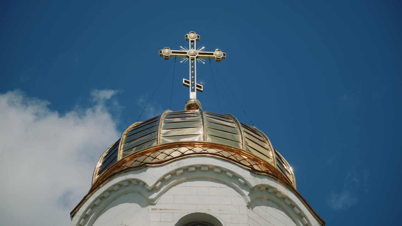 Architektonický detail kostelní kupole zakončené zářícím pravoslavným křížem za jasného denního světla.