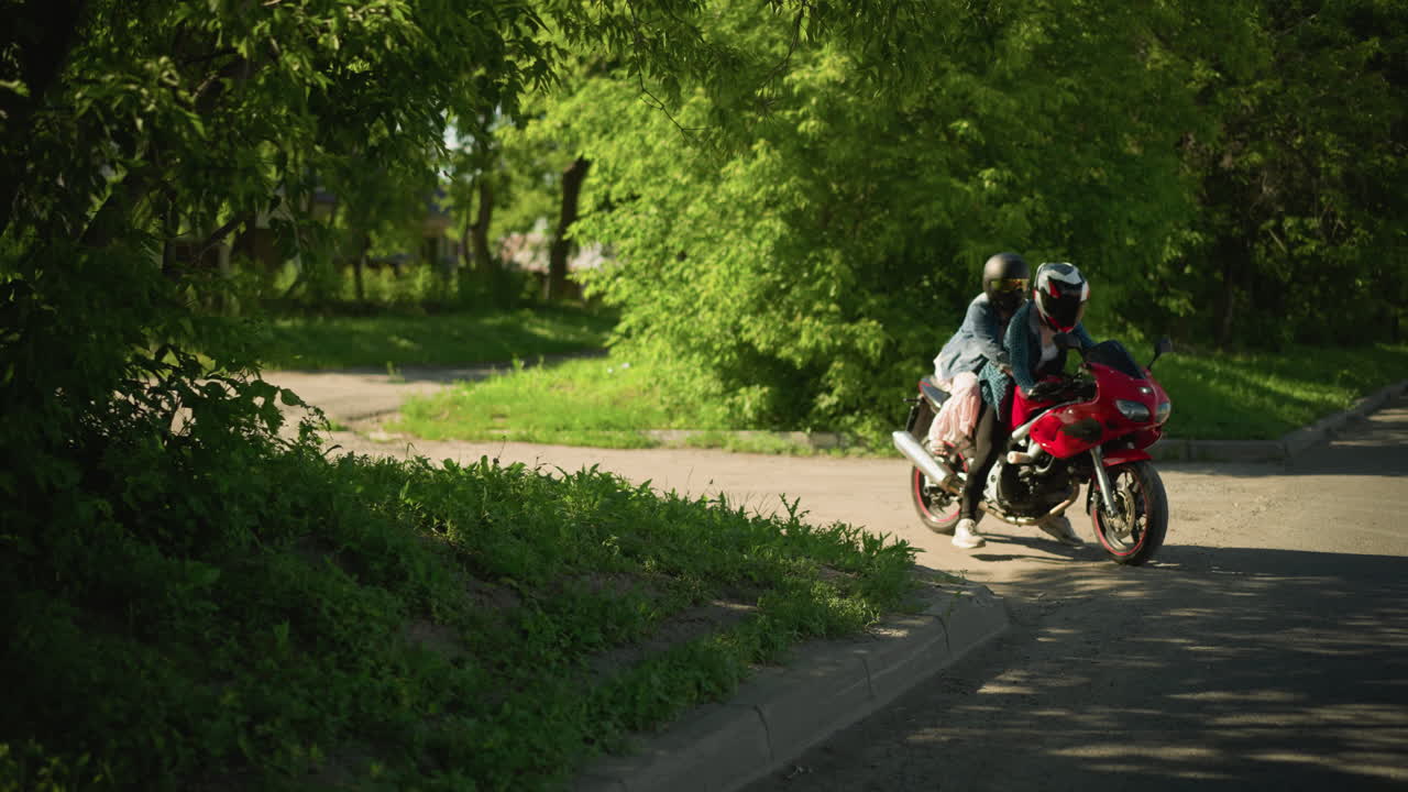 체크색 셔츠를 입은 한 여성이 은 파워 자전거를 타고 그녀의 친구와 함께 뒤에서 그녀를 붙잡고, 그들은 차가 지나가는 그림자 길을 타고, 일부는 헤드라이트를 켜고 있습니다.