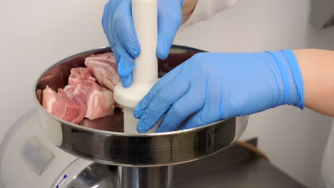 the butcher puts large pieces of pork belly into the meat grinder