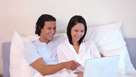 pareja sentada en la cama con una computadora portátil