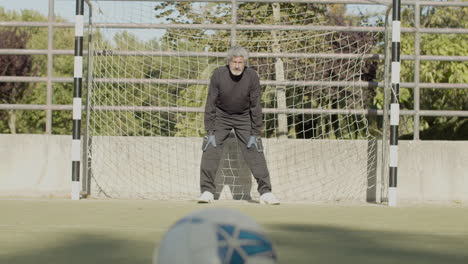 konzentrierter älterer torhüter, der das fußballtor verteidigt und den ball fängt