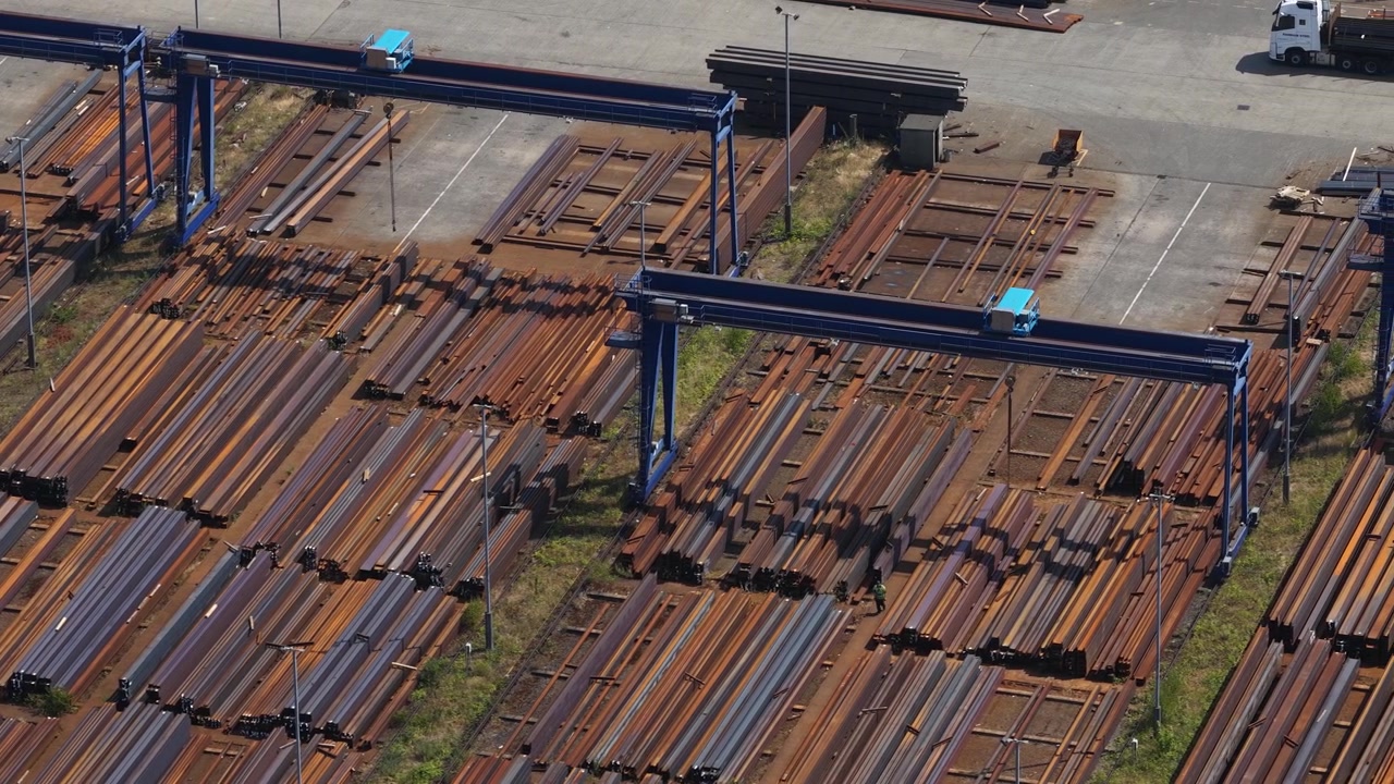 Vista aerea di un magazzino industriale che stocca lastre d'acciaio con gru, adiacente a un grande impianto di produzione dell'acciaio nel Regno Unito.