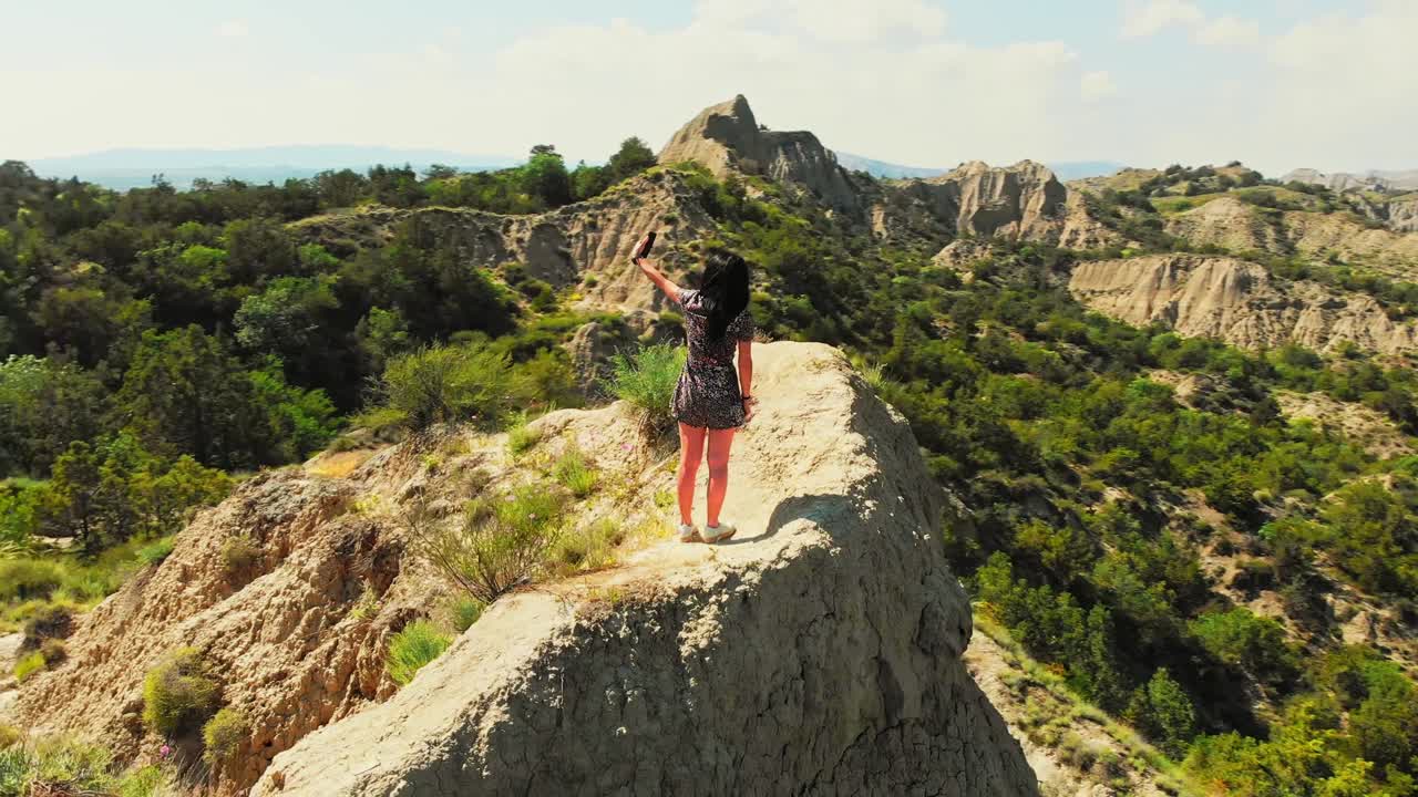 drone disparó a una joven caucásica de pie en la cima de la montaña. turista usando teléfono inteligente para hacerse una selfie juntos en el punto de vista. disparo aéreo, naturaleza, concepto de viaje y aventura.