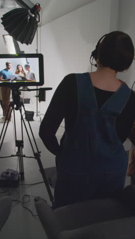 vertical video of actors with scripts in rehearsal with female film director shooting movie or video in studio with film crew and watching on monitor