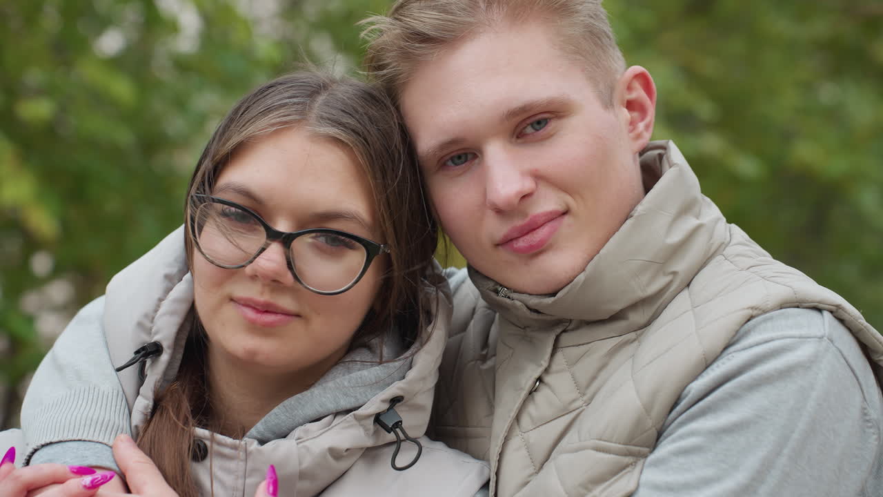 Wonderful moment of couple standing closely outdoors in matching outfits, sharing subtle smiles while trees sway gently in background