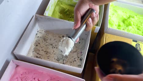 a hand scoops ice cream into a bowl in a brightly lit shop, capturing the vibrant colors and textures of various flavors