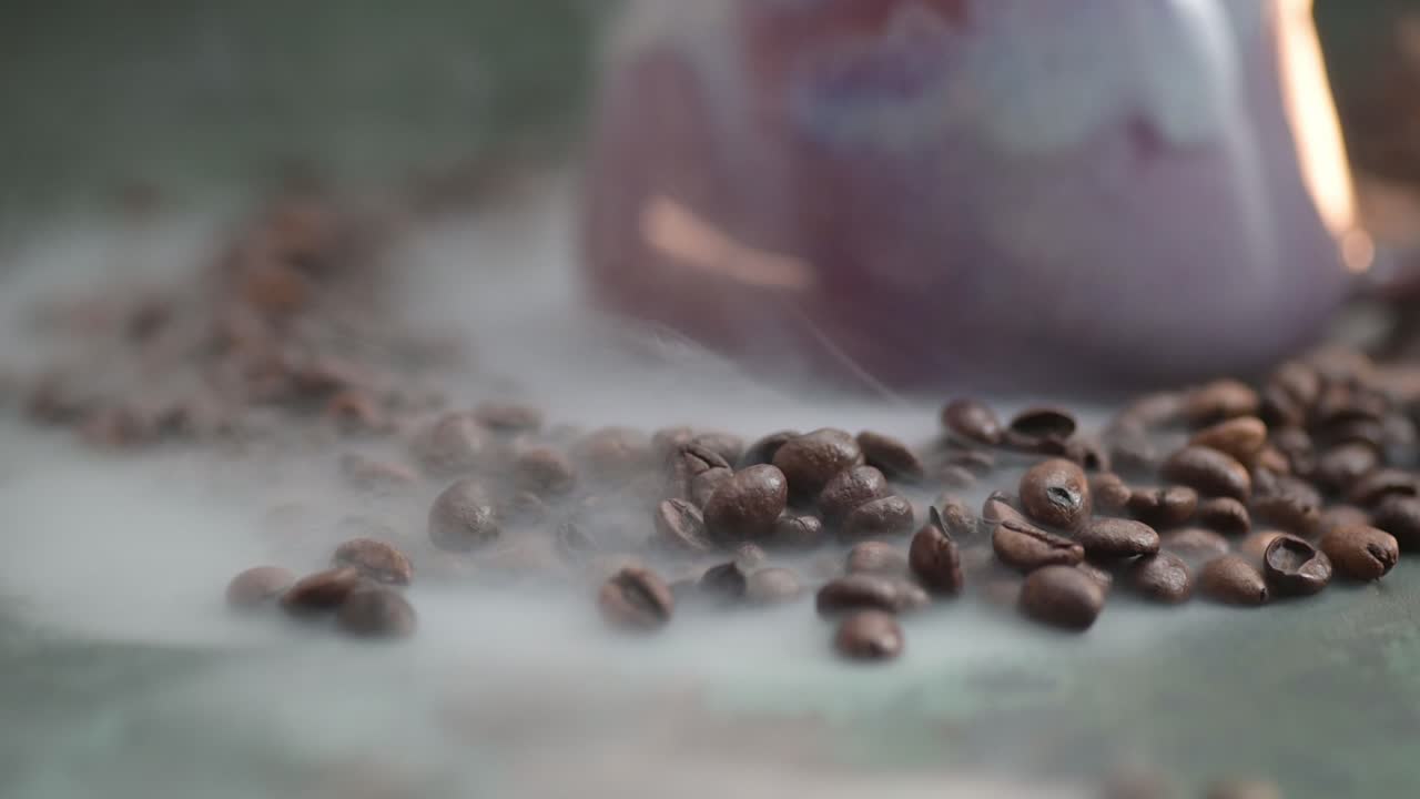 담배의 매크로를 밀어주고, 보라색 컵 위에 떠다니며, 컵은 테이블 위에 놓인 커피 콩으로 둘러싸여 있습니다.