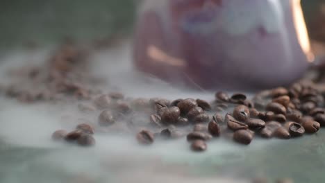 Push-in-macro-of-a-smoke-drifts-over-the-lilac-cup,-mug-surrounded-by-laying-on-the-table-coffee-beans