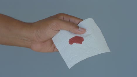 hand holding a tissue with a blood stain