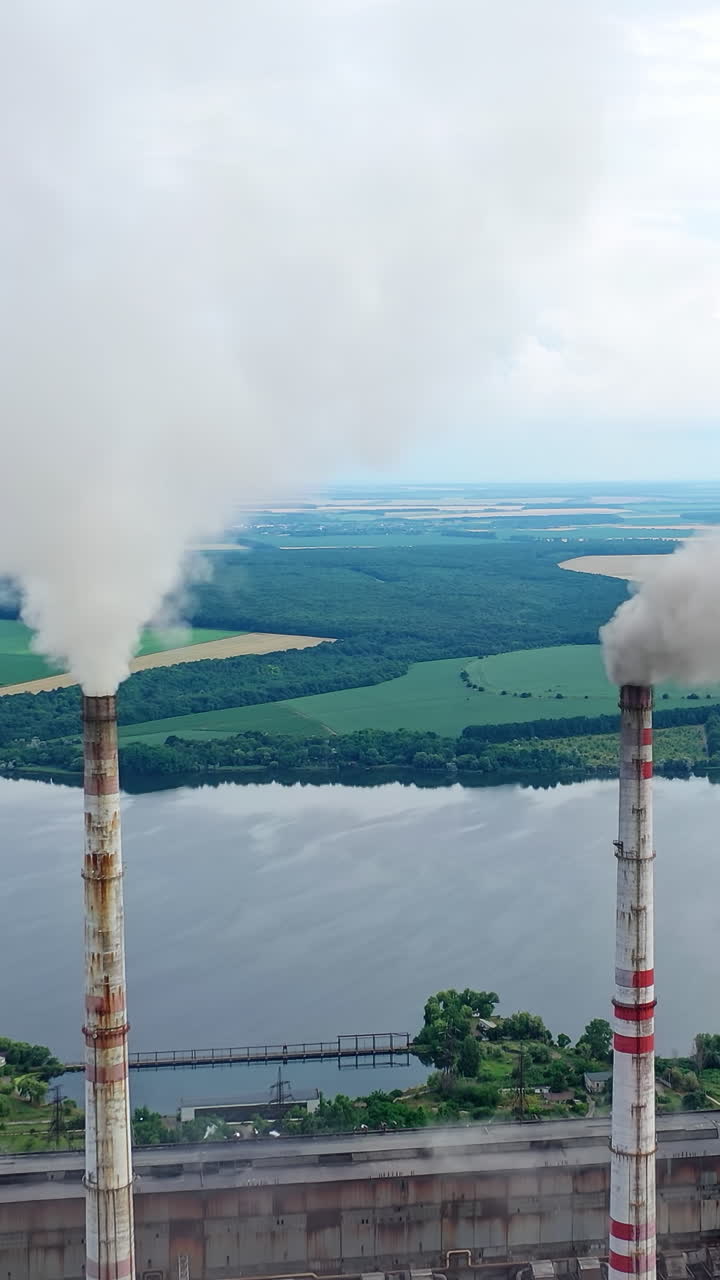 White stack of smoke coming out from large chimneys. Factory chimneys releases harmful emissions into the atmosphere on nature backdrop.Environmental problems. Vertical video