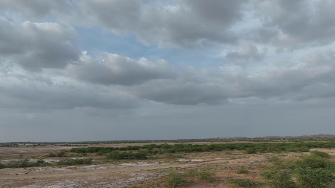 Aerial drone fast moving shot over arid wilderness with few bushes in Nagarparkar, Sindh, Pakistan on a cloudy day