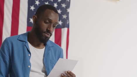 Man-Stands-In-Front-Of-USA-Flag-At-American-Election-Deciding-How-To-Cast-His-Vote