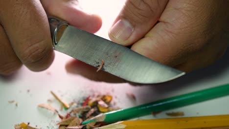 imágenes de manos afilando lentamente un lápiz y algunos lápices de colores con un cuchillo afilado