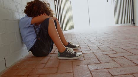 side view of mixed-race schoolgirl sitting alone on the floor in corridor at school 4k