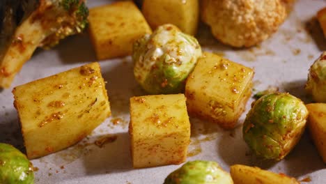 a close up shot of an assortment of fresh vegetables covered in a layer of tasty seasoning on a baking tray, the vegetables have been prepared on a sheet of non stick parchment paper before roasting