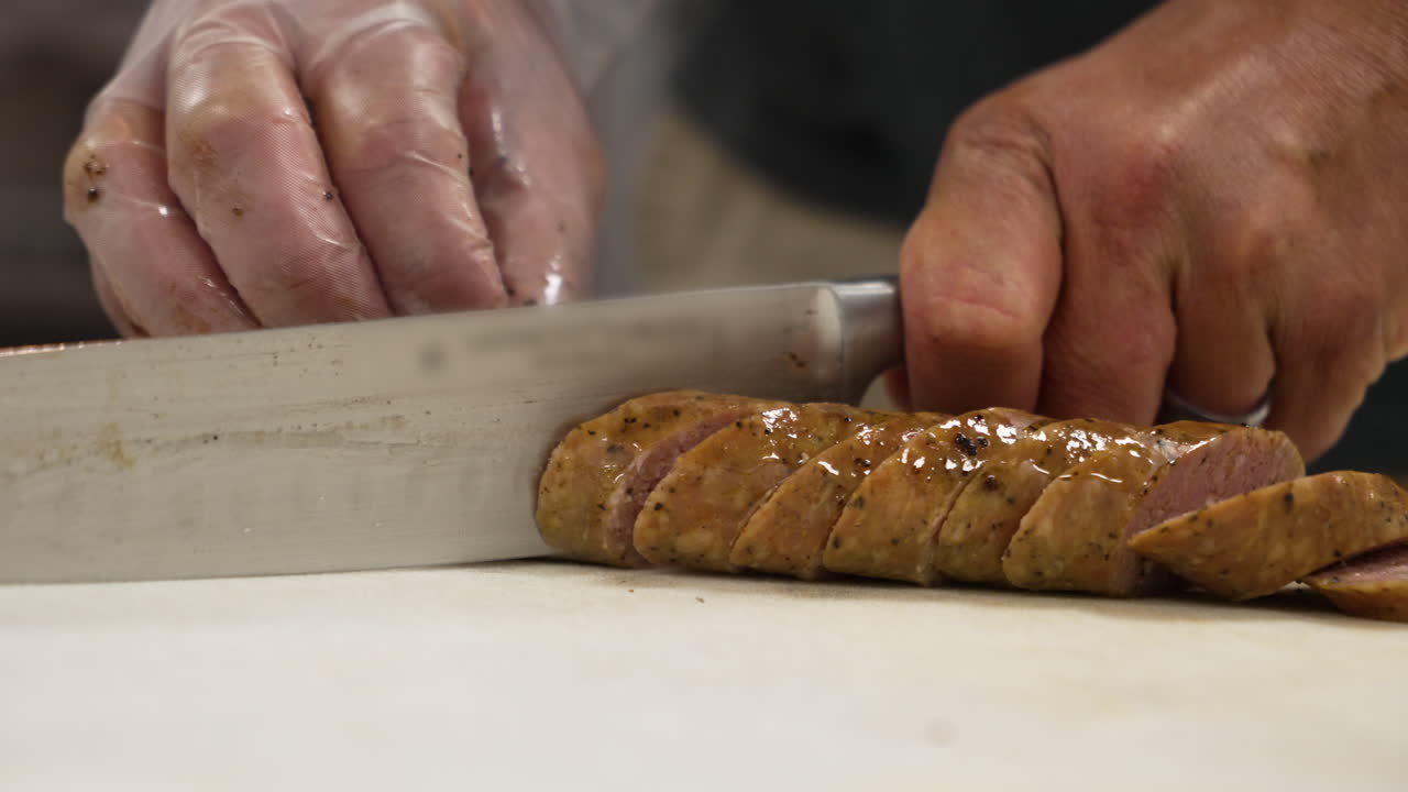 Pitmaster slices Texas style smoked barbecue sausage into equal angled coin rounds, slow motion close up 4K