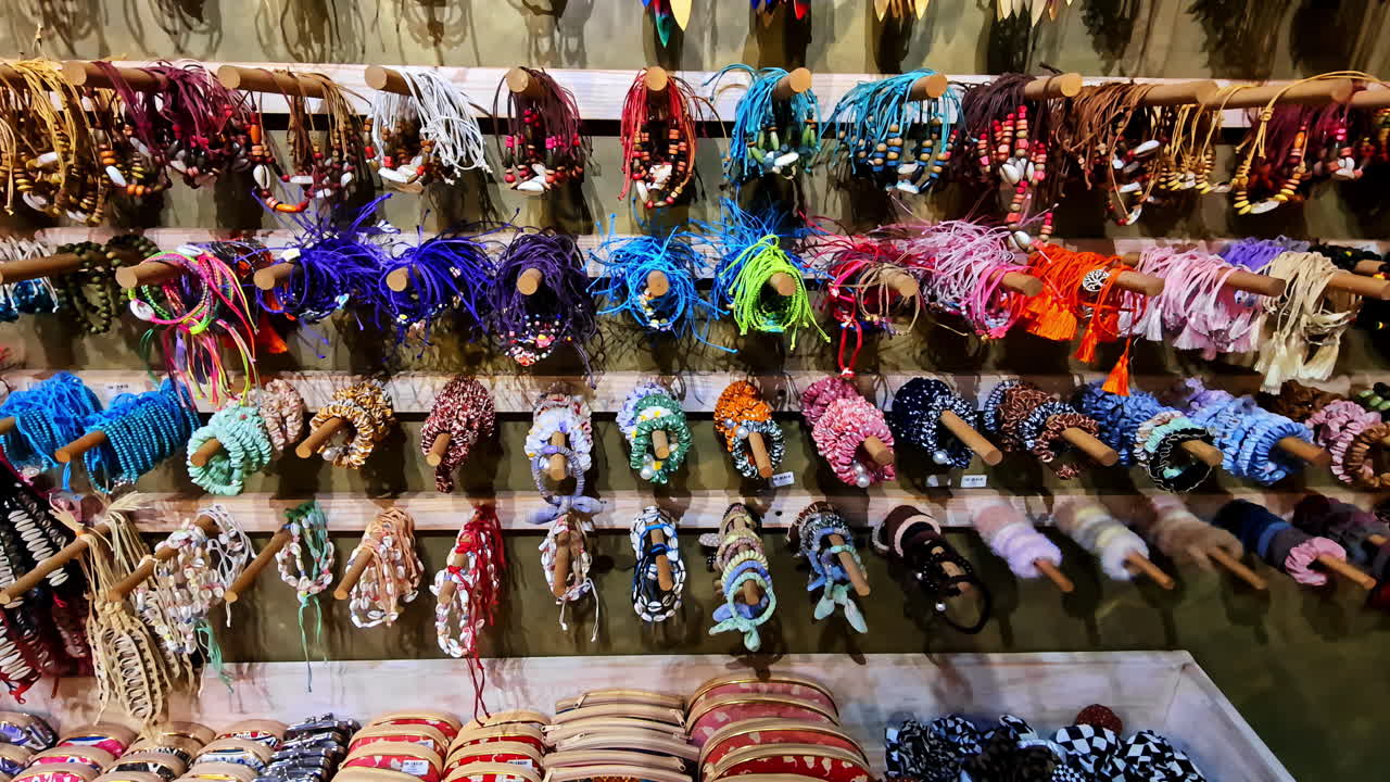 A vibrant collection of colorful, locally made woven bracelets, necklaces, and souvenirs hangs on a display wall at a traditional craft market stall in Ella, Sri Lanka