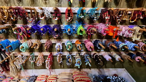 a vibrant collection of colorful, locally made woven bracelets, necklaces, and souvenirs hangs on a display wall at a traditional craft market stall in ella, sri lanka