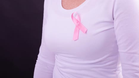 Video-of-midsection-of-caucasian-woman-wearing-pink-cancer-awareness-ribbon,-with-black-background