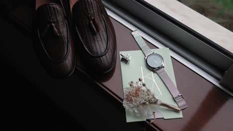 groom's shoes watch cufflinks and boutonniere by window in natural light