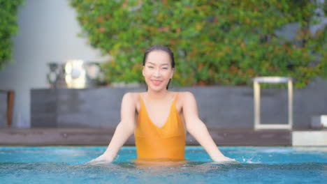 Mujer-Asiática-Infantil-En-La-Piscina-Rociando-Agua-Y-Mirando-A-La-Cámara,-Fotograma-Completo