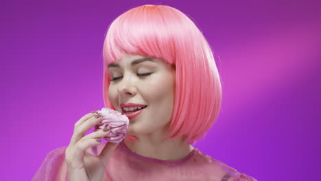 close up of cute woman eating little cake with pink cream and smiling