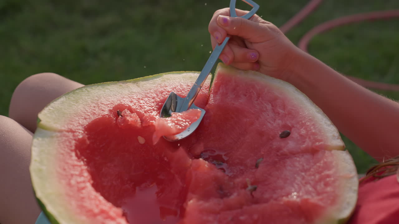 Sunlit Backyard Person Scooping Watermelon With Spoon On Lap, Red Flesh Dotted With Black Seeds, Green Rind Cradled By Hands, Wooden Bench Under Warm Afternoon Light, Sticky Juice Glistening, Casual