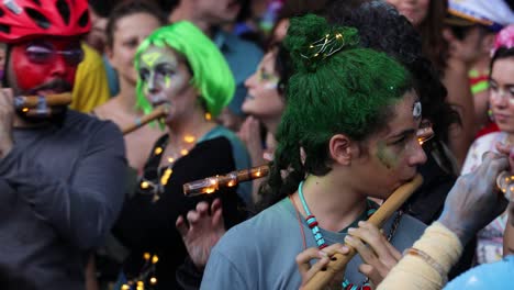 group of young people painted face and hair in vivid colours playing transverse flute and singing and dancing