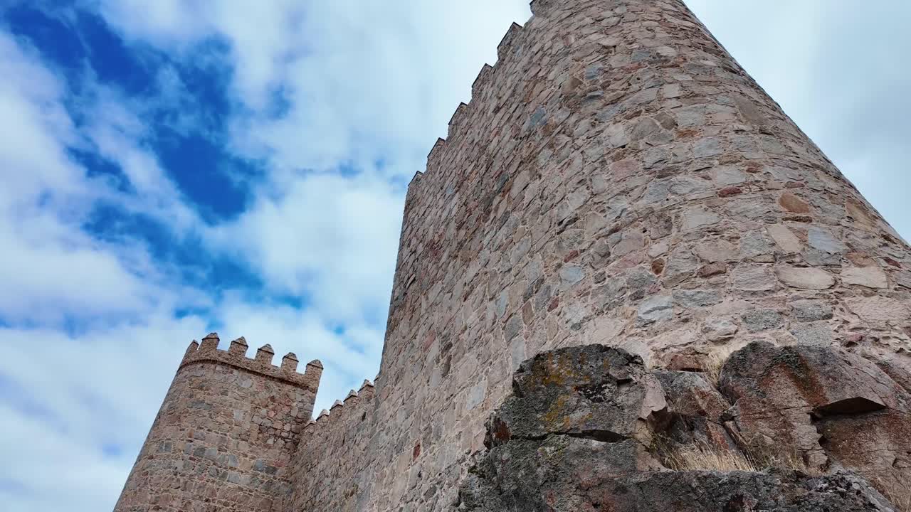 Ampia veduta delle storiche mura medievali di Ávila, Spagna, che si estendono su una collina erbosa sotto un cielo nuvoloso e drammatico. Una delle città fortificate meglio conservate d'Europa e un sito patrimonio UNESCO.